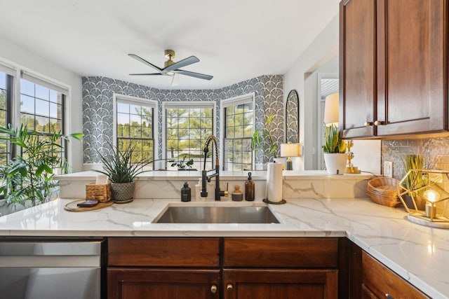 kitchen featuring sink, light stone counters, stainless steel dishwasher, ceiling fan, and backsplash