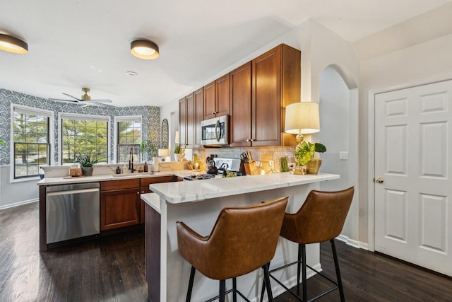 kitchen featuring a kitchen bar, sink, appliances with stainless steel finishes, dark hardwood / wood-style floors, and kitchen peninsula