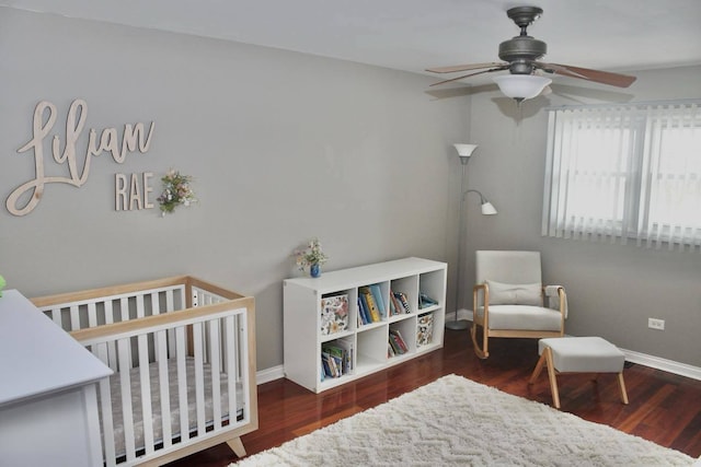 bedroom featuring a nursery area, dark wood-type flooring, and ceiling fan