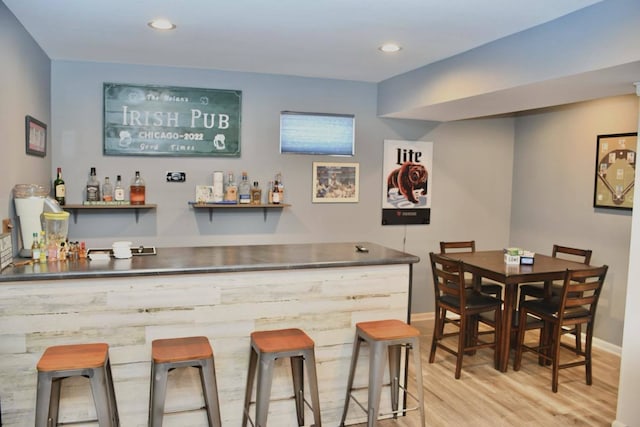 bar with light hardwood / wood-style floors and stainless steel counters