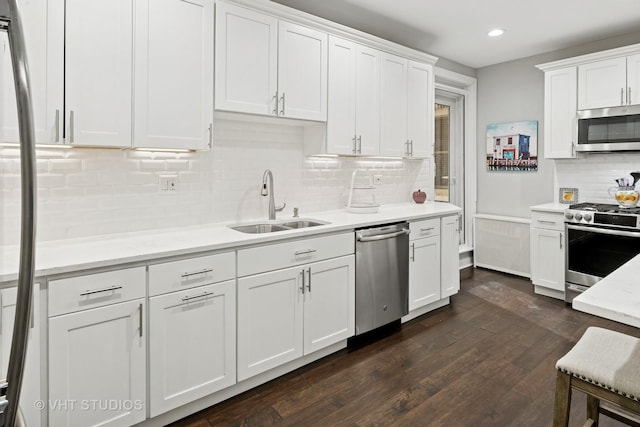 kitchen with a sink, white cabinetry, appliances with stainless steel finishes, dark wood-style floors, and tasteful backsplash