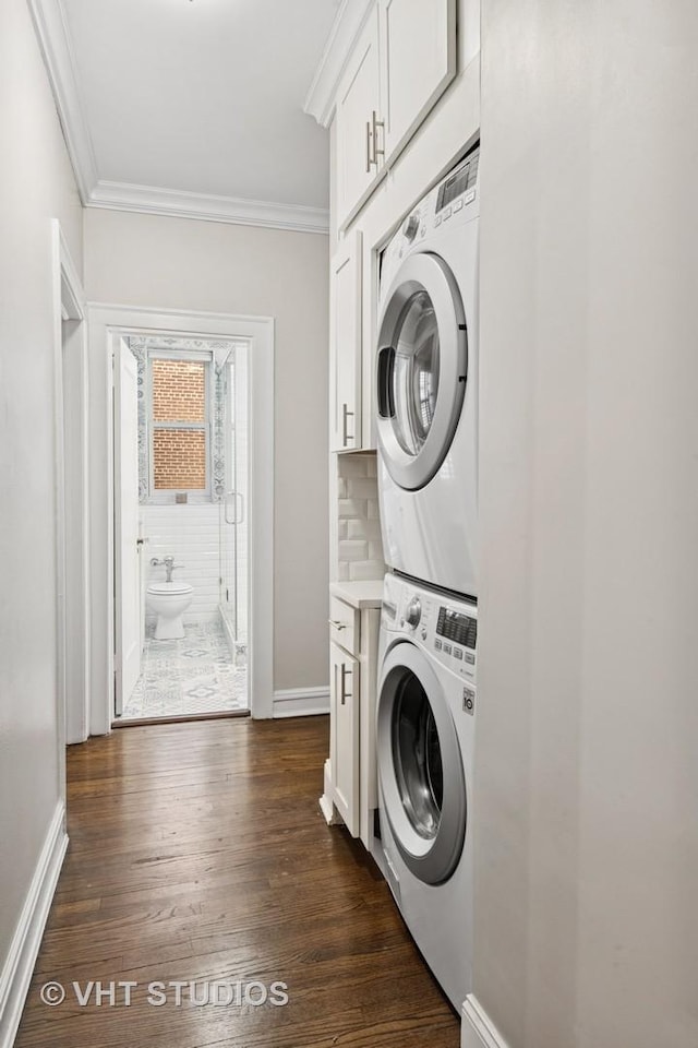 clothes washing area featuring stacked washing maching and dryer, dark wood-style floors, cabinet space, and ornamental molding