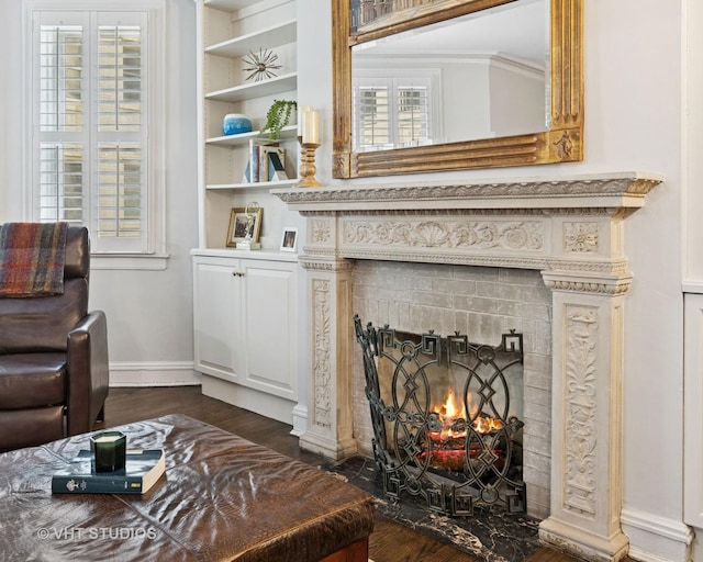 sitting room with a warm lit fireplace, dark wood-type flooring, built in shelves, and baseboards