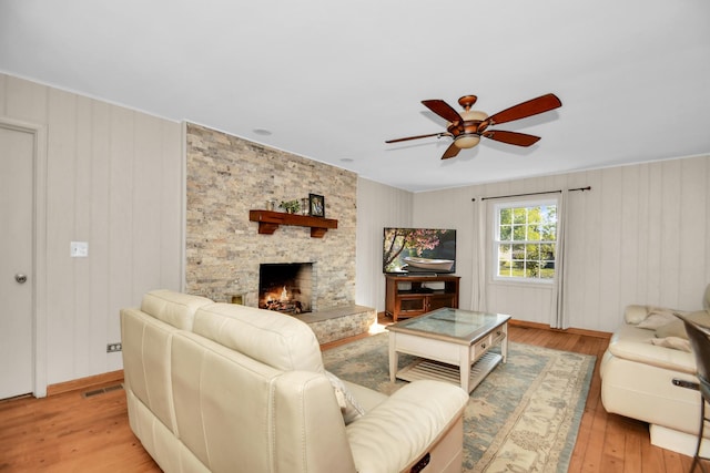 living room featuring ceiling fan, a stone fireplace, and light wood-type flooring