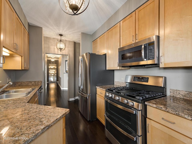 kitchen featuring stainless steel appliances, decorative light fixtures, a sink, and light brown cabinets