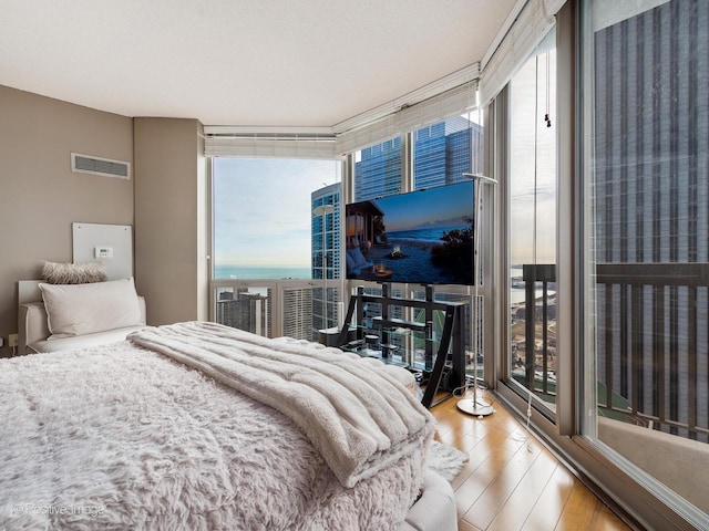 bedroom with access to exterior, floor to ceiling windows, visible vents, and wood finished floors