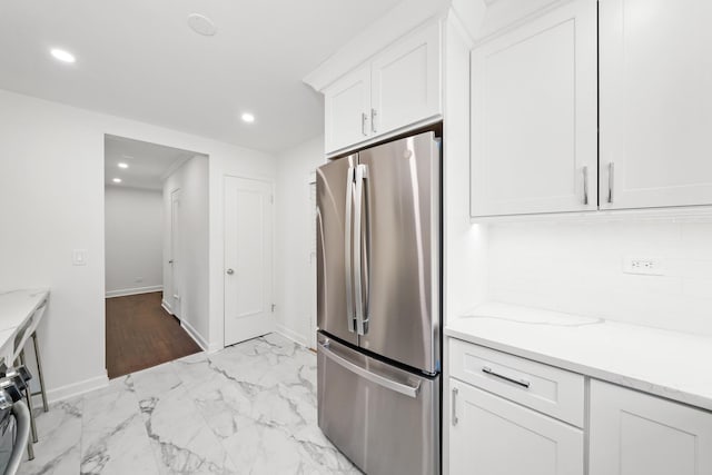 kitchen with white cabinetry, light stone counters, stainless steel fridge, and tasteful backsplash