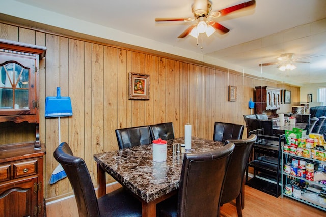 dining area with ceiling fan, wood walls, and light wood-type flooring