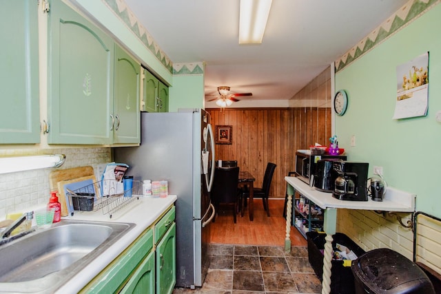 kitchen featuring stainless steel refrigerator, wood walls, sink, green cabinets, and ceiling fan