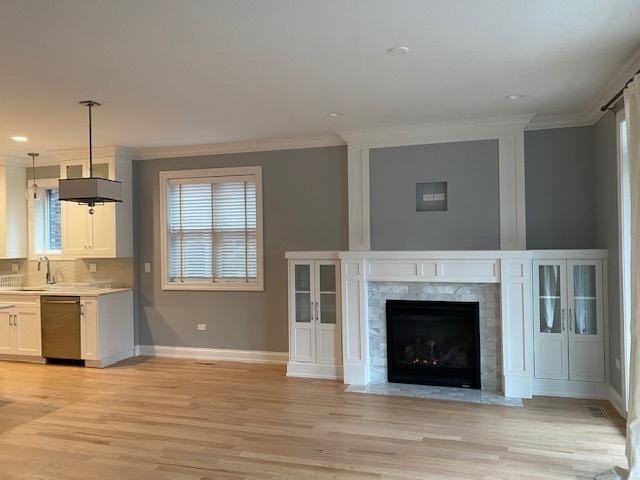 unfurnished living room featuring sink, crown molding, a fireplace, and light hardwood / wood-style floors