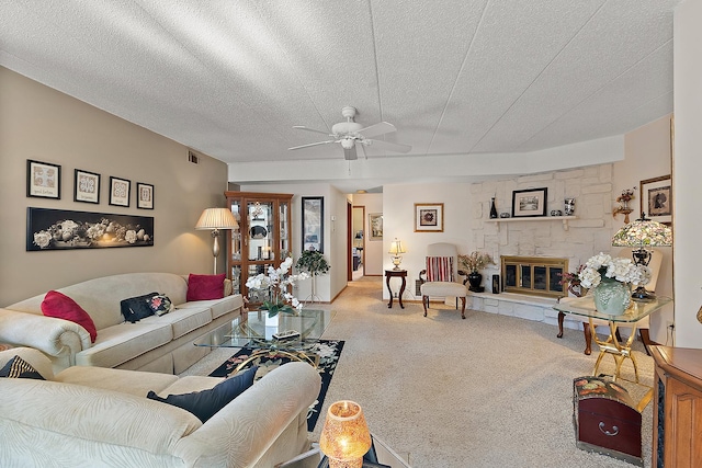 carpeted living room with ceiling fan, a stone fireplace, and a textured ceiling