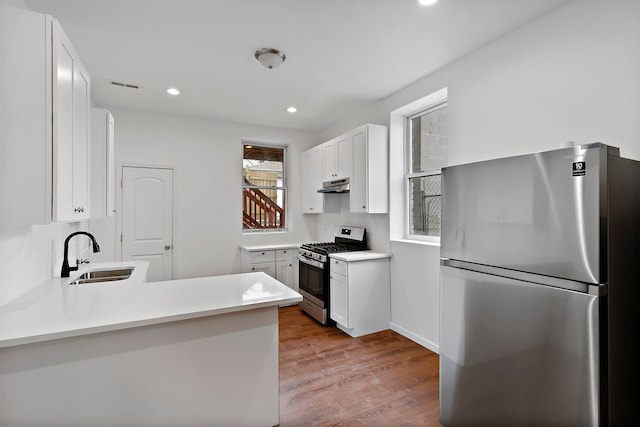 kitchen with sink, appliances with stainless steel finishes, white cabinetry, light hardwood / wood-style floors, and kitchen peninsula