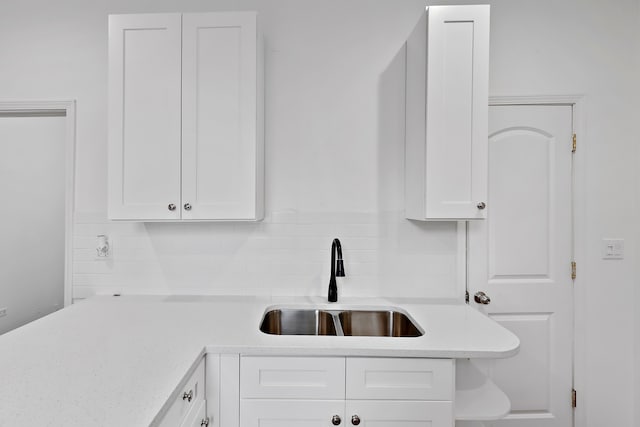 kitchen featuring tasteful backsplash, white cabinetry, light stone countertops, and sink