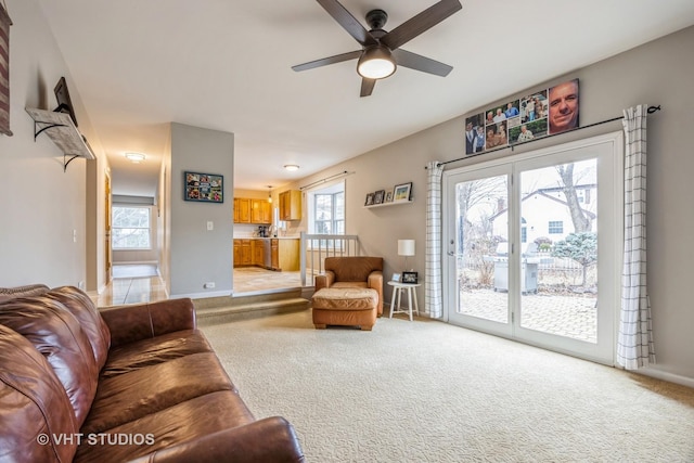 living area featuring baseboards, a ceiling fan, and light colored carpet