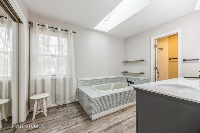 full bathroom with a garden tub, double vanity, visible vents, a sink, and wood finished floors