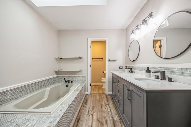 bathroom with decorative backsplash, toilet, a sink, wood finished floors, and a bath