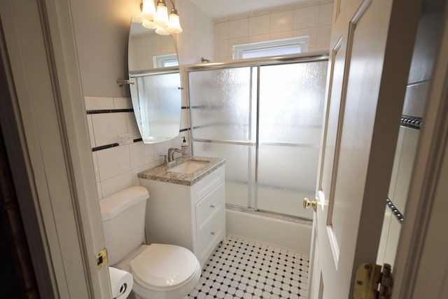 full bathroom featuring enclosed tub / shower combo, tile walls, vanity, and toilet