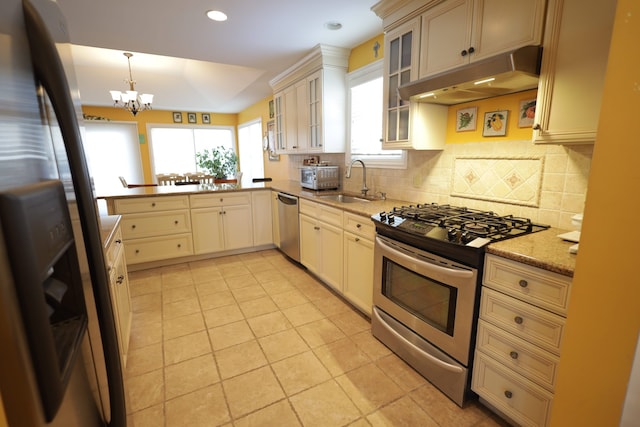 kitchen with light tile patterned flooring, appliances with stainless steel finishes, sink, hanging light fixtures, and light stone counters