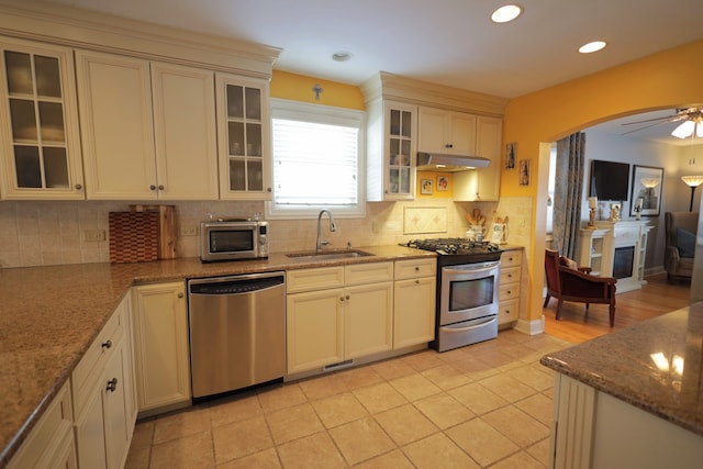 kitchen with appliances with stainless steel finishes, sink, backsplash, and light stone counters