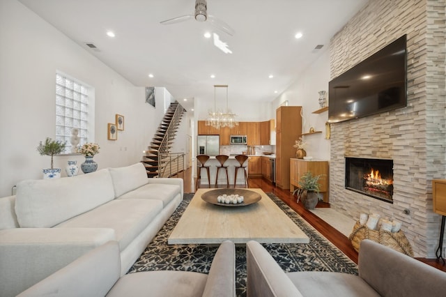 living room featuring hardwood / wood-style flooring, a stone fireplace, and ceiling fan with notable chandelier