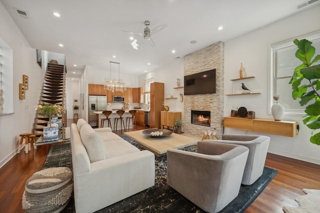 living room with dark wood-type flooring, ceiling fan, and a stone fireplace