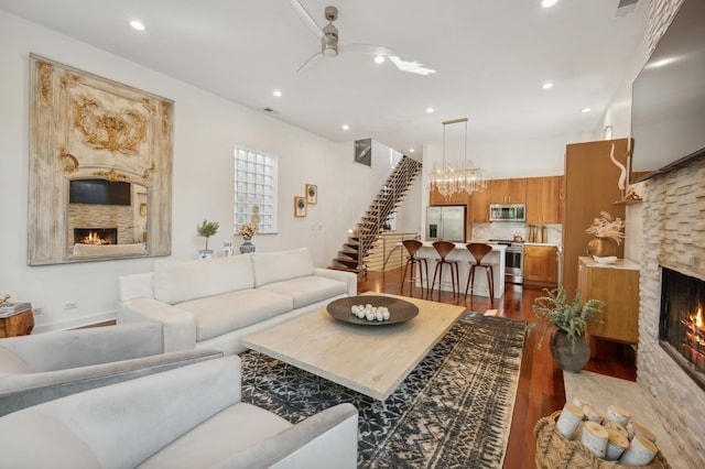 living room featuring a stone fireplace, dark wood-type flooring, and ceiling fan