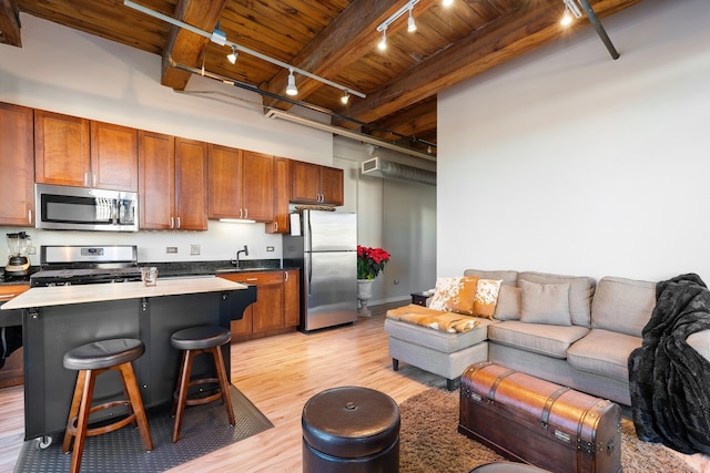 kitchen with beamed ceiling, a breakfast bar area, stainless steel appliances, a center island with sink, and wooden ceiling