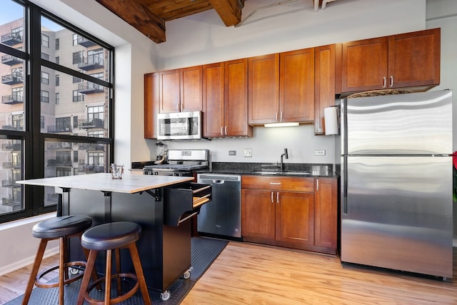 kitchen with appliances with stainless steel finishes, sink, beam ceiling, and light hardwood / wood-style flooring