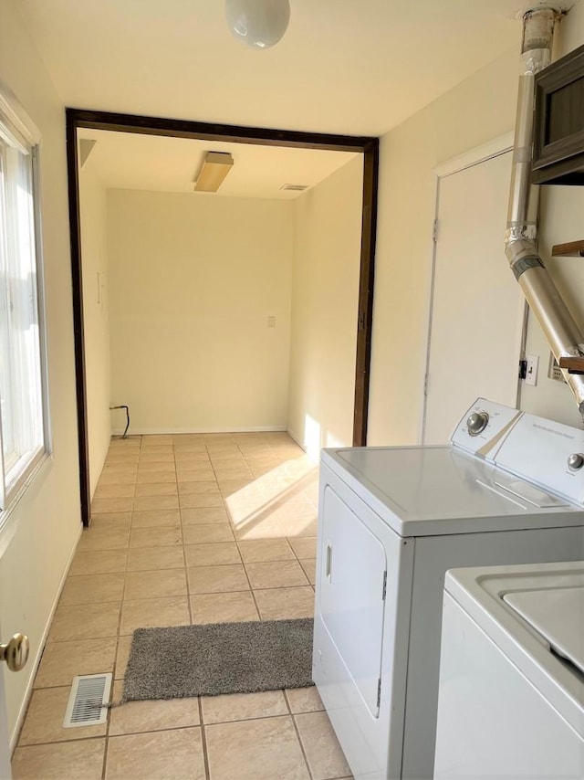 clothes washing area with plenty of natural light, washer and dryer, and light tile patterned floors