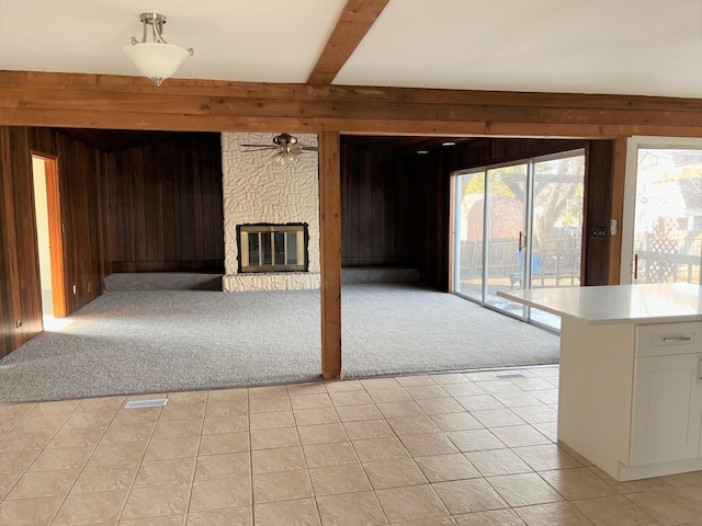 unfurnished living room featuring light carpet, a stone fireplace, wooden walls, and beam ceiling