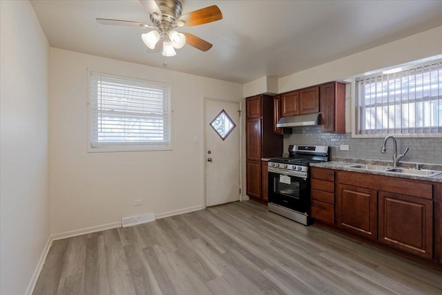 kitchen with sink, stainless steel gas range oven, tasteful backsplash, light wood-type flooring, and ceiling fan