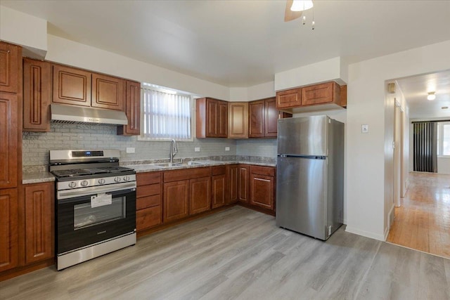 kitchen featuring sink, light wood-type flooring, stainless steel appliances, light stone countertops, and decorative backsplash