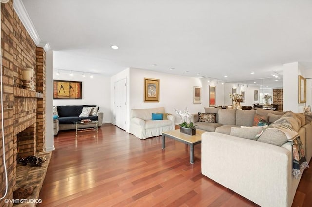 living room featuring crown molding, a brick fireplace, dark hardwood / wood-style floors, and rail lighting