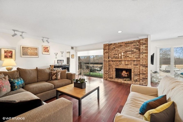 living room with dark wood-type flooring, track lighting, and a brick fireplace