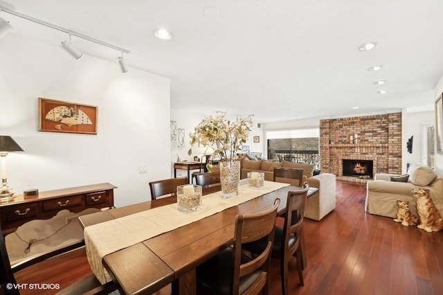 dining space with rail lighting, a brick fireplace, and dark wood-type flooring