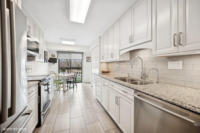 kitchen with white cabinetry, sink, backsplash, stainless steel appliances, and light stone countertops