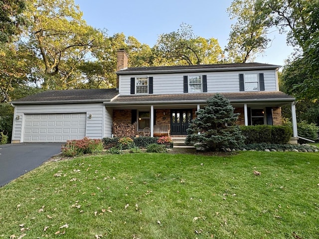 traditional-style house with an attached garage, covered porch, driveway, a front lawn, and a chimney