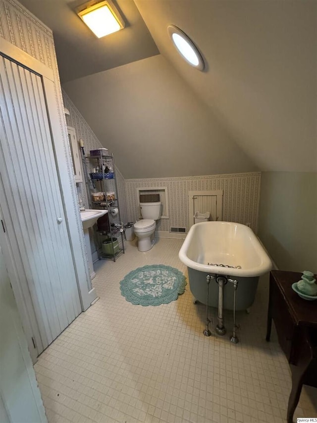 bathroom featuring a tub to relax in, vaulted ceiling, and toilet