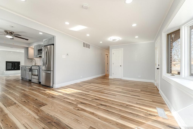 spare room with ceiling fan, light hardwood / wood-style flooring, a large fireplace, and crown molding