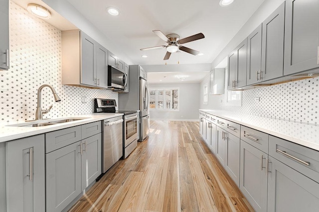 kitchen with appliances with stainless steel finishes, decorative backsplash, light hardwood / wood-style floors, gray cabinets, and sink