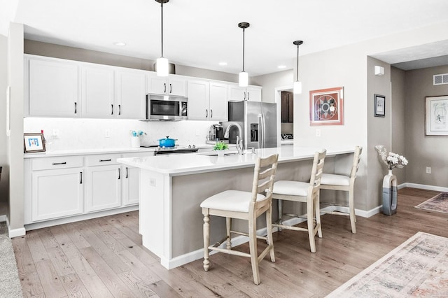 kitchen with stainless steel appliances, hanging light fixtures, a kitchen island with sink, and white cabinets