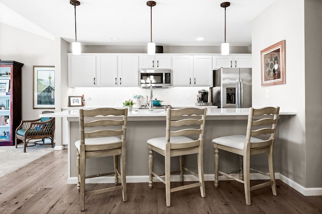 kitchen with pendant lighting, a kitchen bar, white cabinetry, and appliances with stainless steel finishes