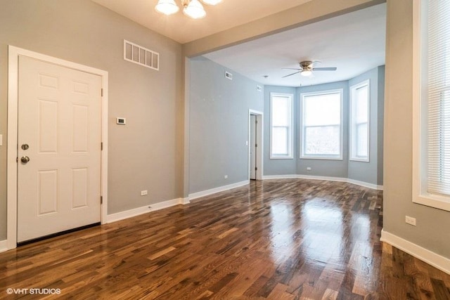 empty room with dark hardwood / wood-style floors and ceiling fan with notable chandelier