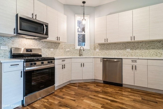 kitchen featuring pendant lighting, dark wood-type flooring, stainless steel appliances, white cabinets, and decorative backsplash