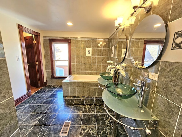 bathroom featuring tiled bath, sink, and tile walls