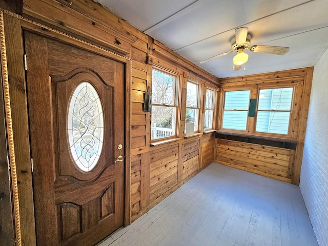 foyer entrance with light hardwood / wood-style flooring, ceiling fan, and wood walls