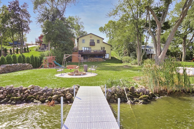 dock area featuring a lawn, a water view, a playground, and an outdoor fire pit