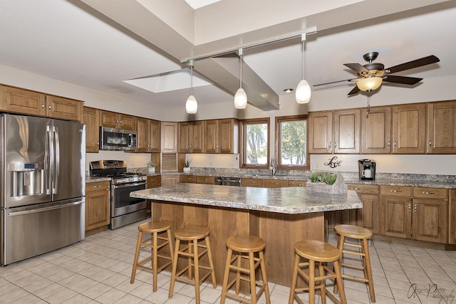 kitchen with sink, a center island, hanging light fixtures, appliances with stainless steel finishes, and a kitchen breakfast bar