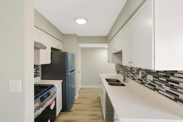 kitchen with appliances with stainless steel finishes, sink, white cabinets, backsplash, and light hardwood / wood-style floors