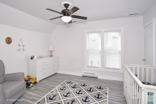 bedroom featuring lofted ceiling, ceiling fan, baseboard heating, a nursery area, and wood-type flooring